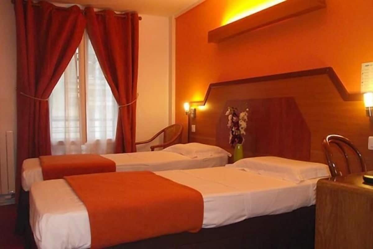 Een hotelkamer met twee bedden, rode gordijnen, een houten hoofdeinde en een nachtkastje met een lamp.