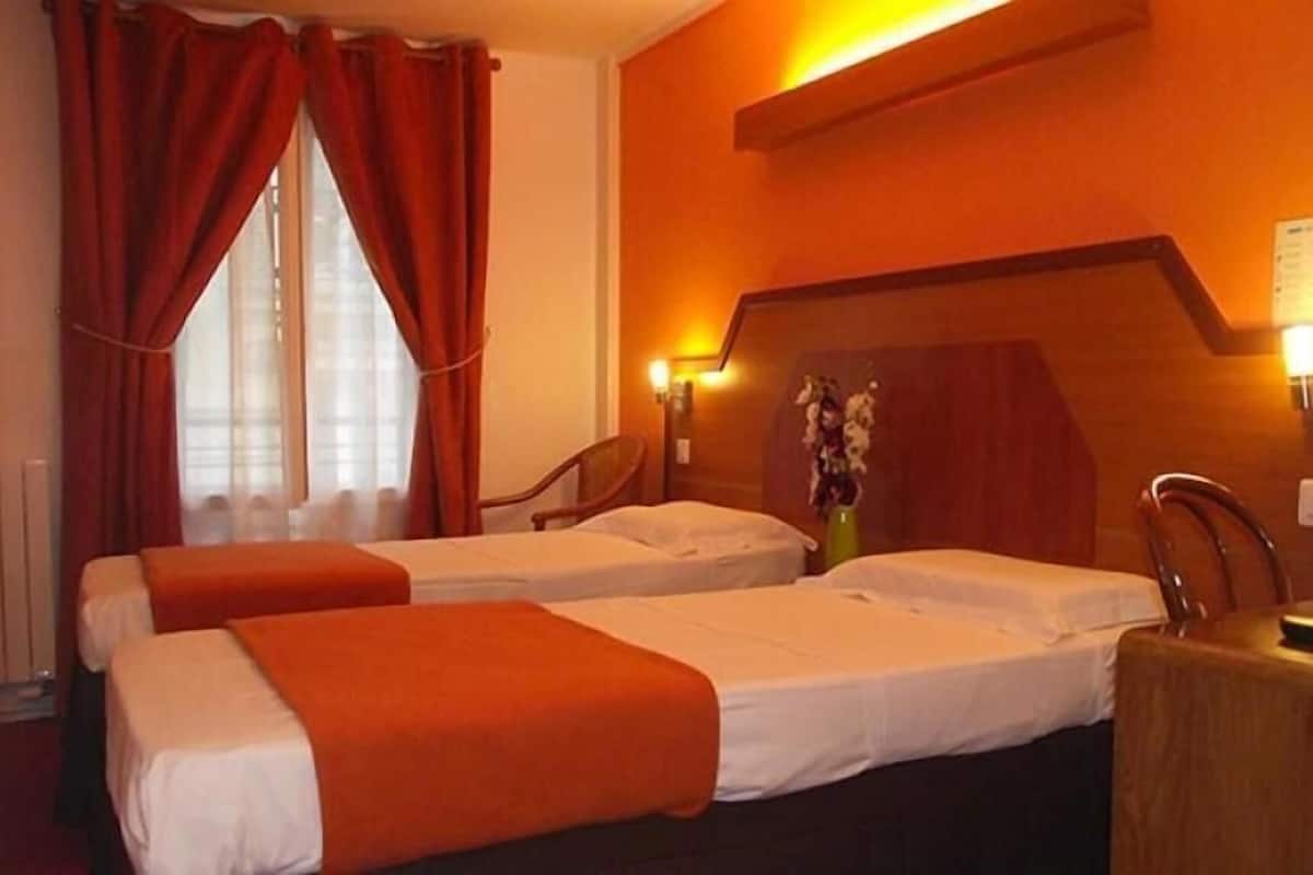 Een hotelkamer met twee bedden, rode gordijnen, een radiator, een houten hoofdeinde en een vaas met bloemen.