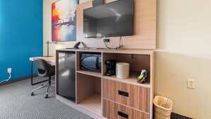 A compact hotel room with a desk, chair, microwave, and a TV mounted on the wall.