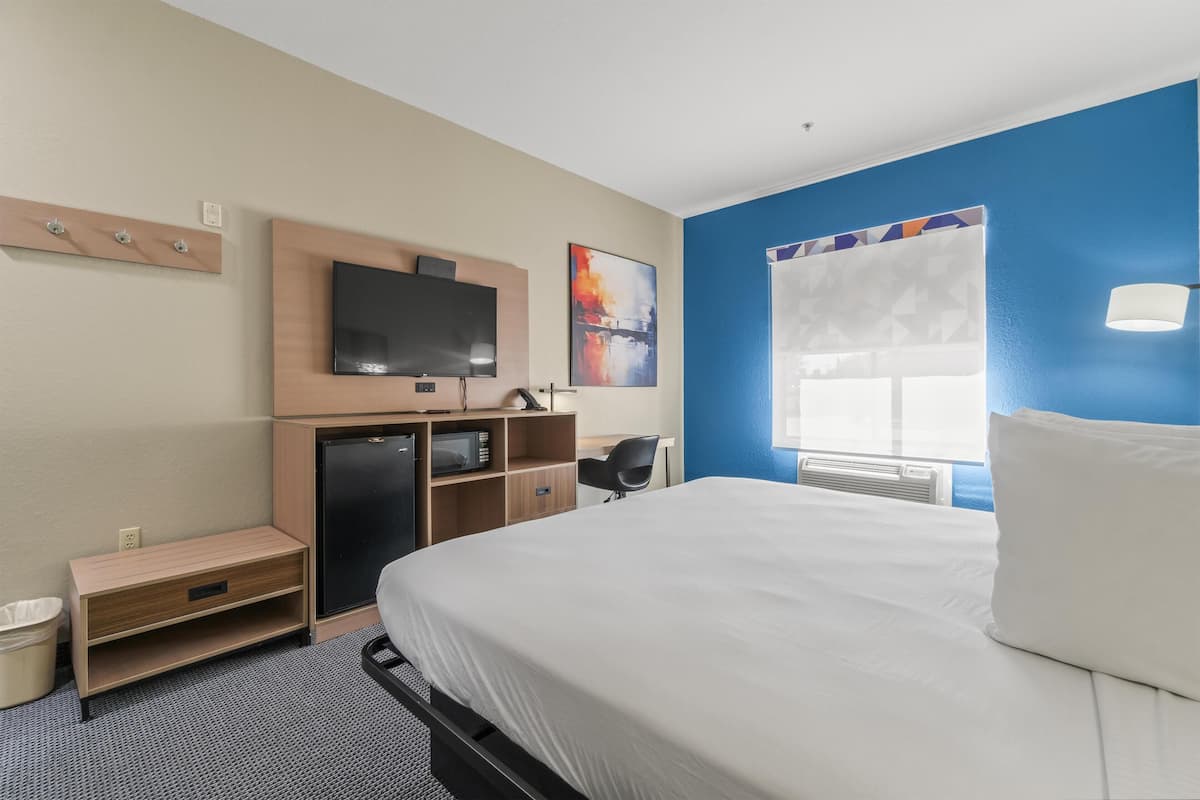 A hotel room with a bed, a desk, a television, and a window with blinds.