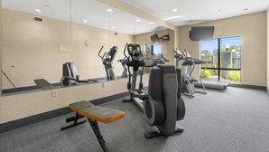 A gym with exercise equipment, a bench, and a large mirror.