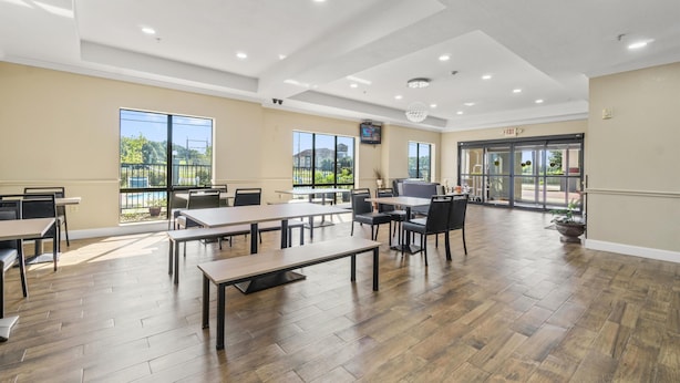 A spacious indoor area with multiple tables and chairs, large windows, and an exit door.