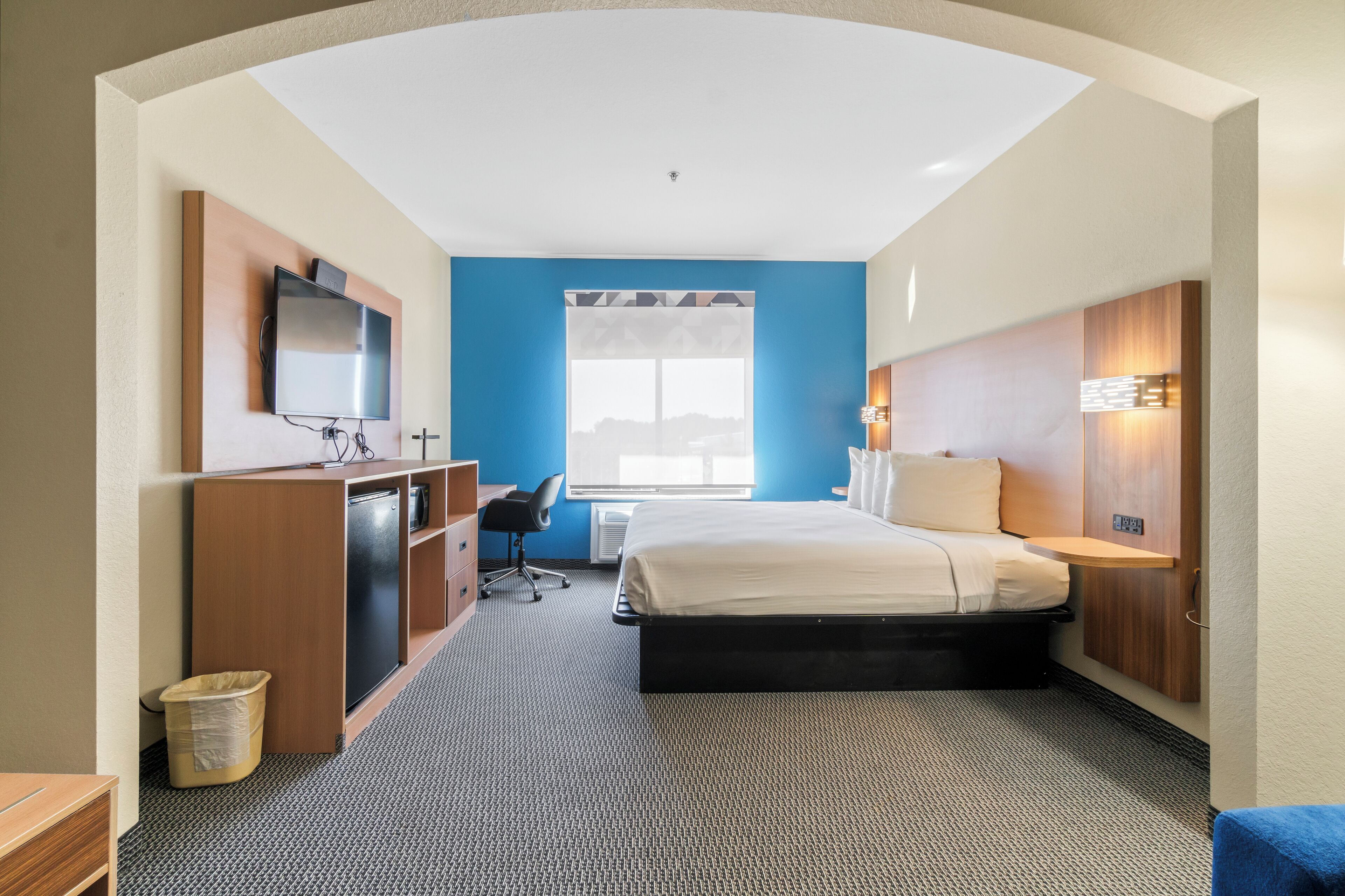 A hotel room with a bed, desk, chair, and a television mounted on the wall.