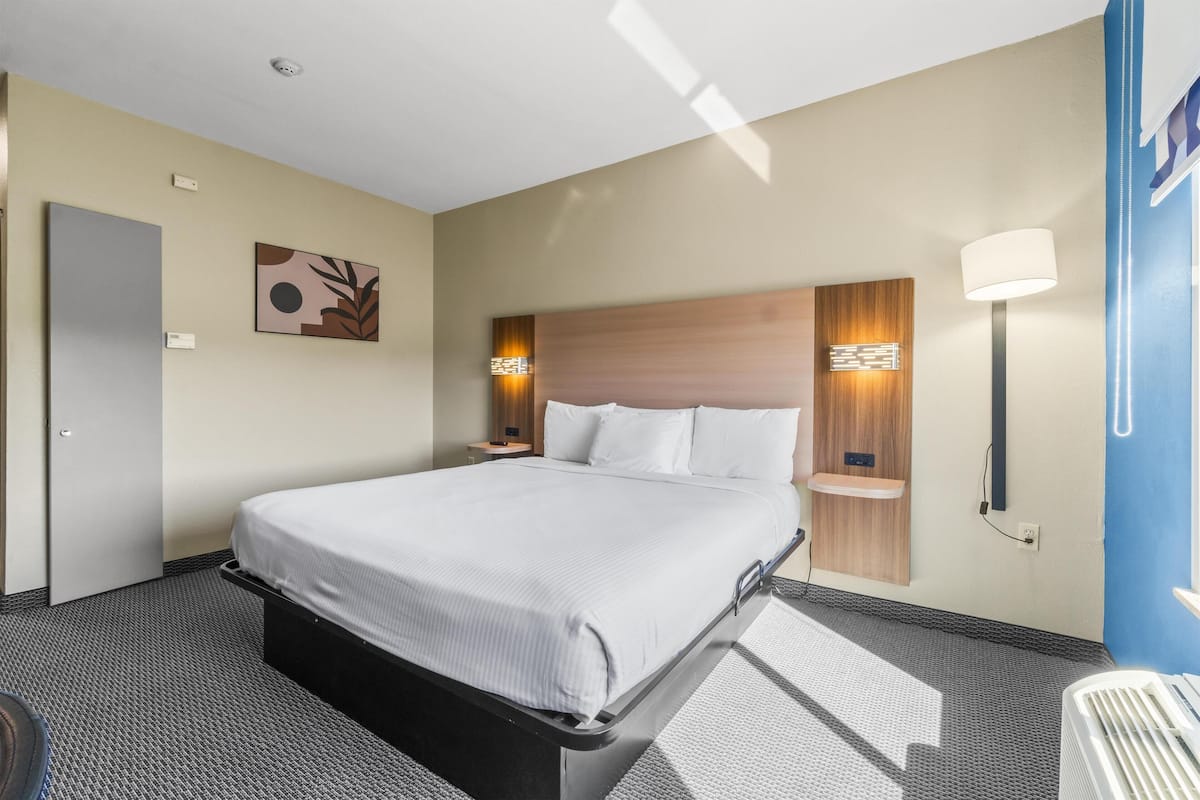 A hotel room with a bed, bedside tables, a wall-mounted lamp, and a door.