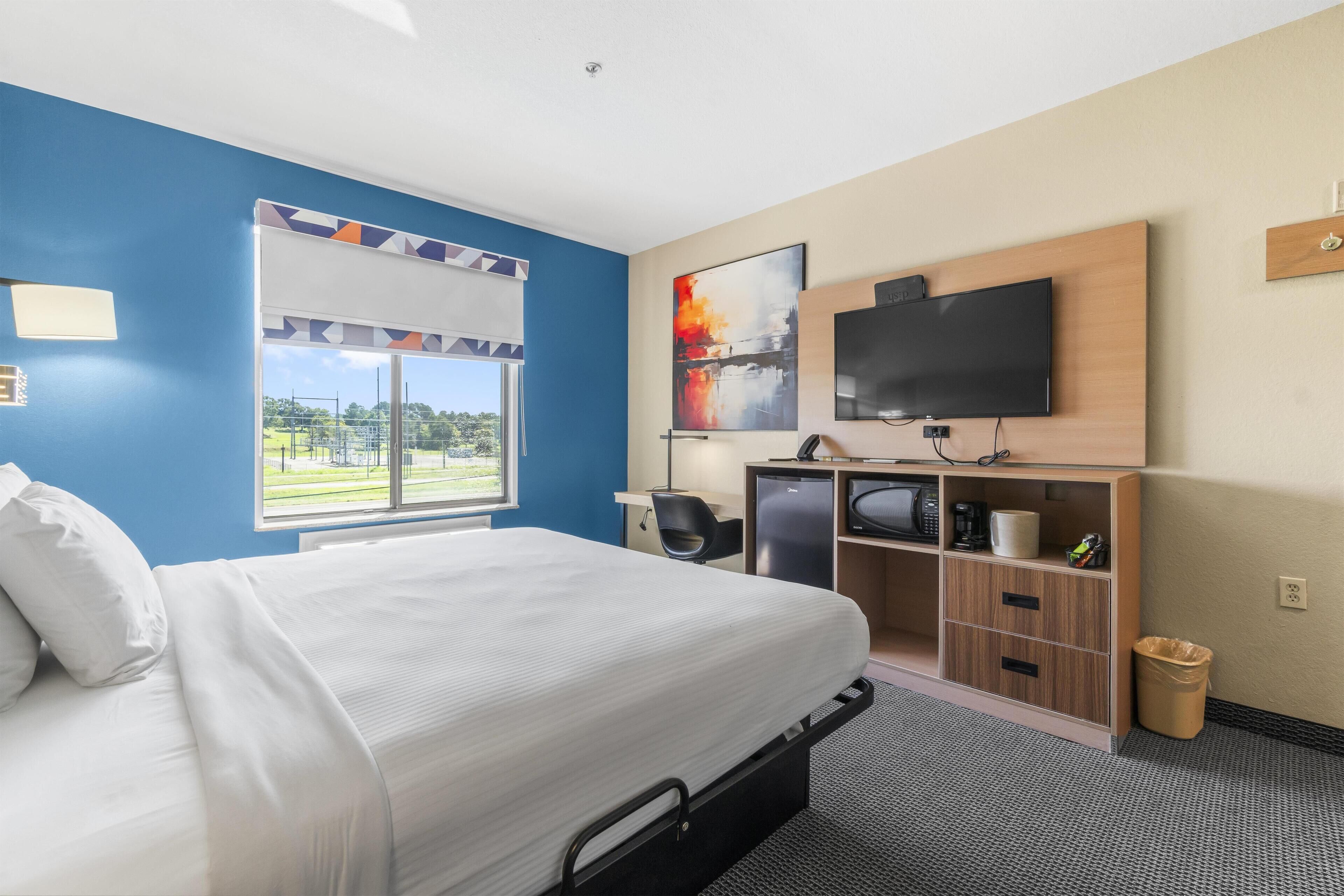 A hotel room with a bed, desk, TV, and a view of the outdoors.