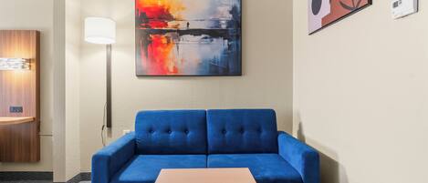 A blue sofa with a small wooden table in front, a painting on the wall, a lamp, and a thermostat.
