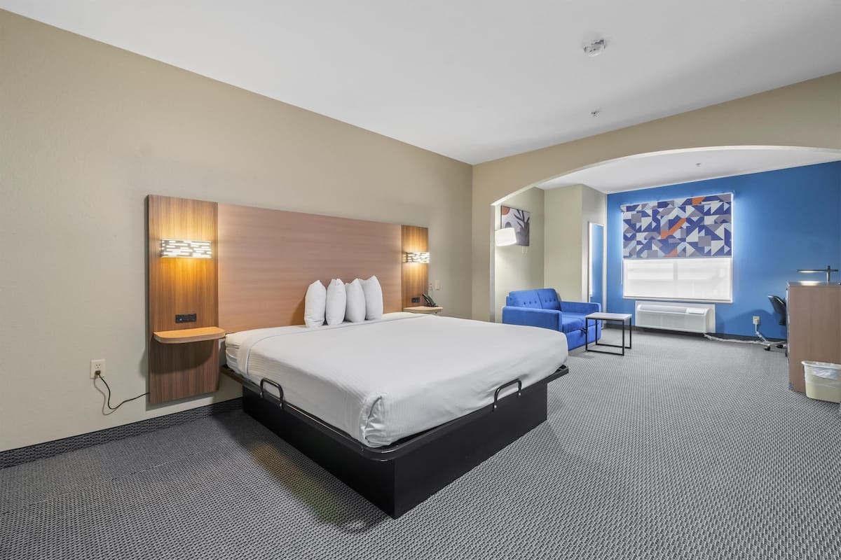 A hotel room with a large bed, a desk, a chair, and a window with a geometric pattern.