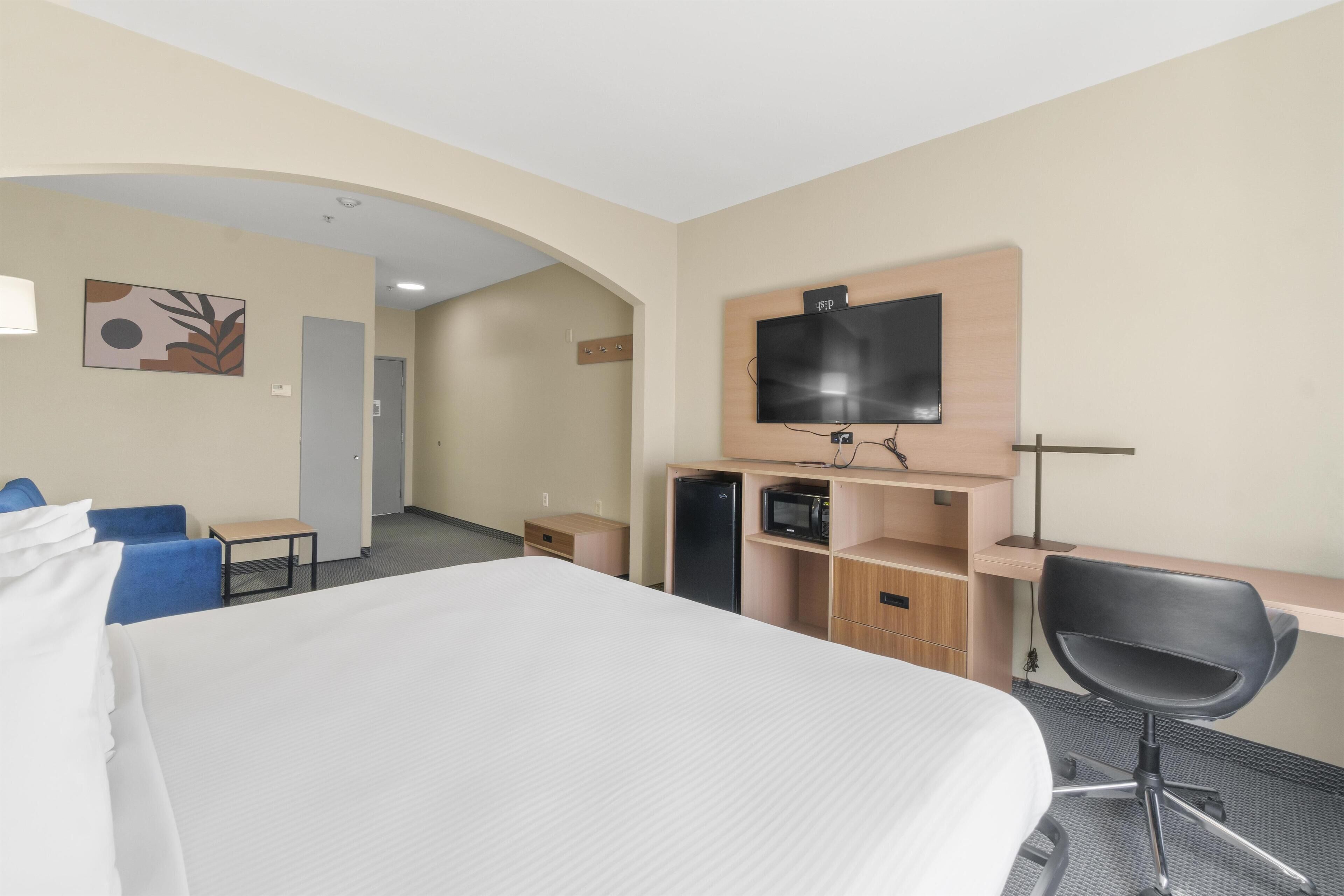 Ett hotellrum med en stor säng, ett skrivbord med en dator, en TV och en mikrovågsugn.