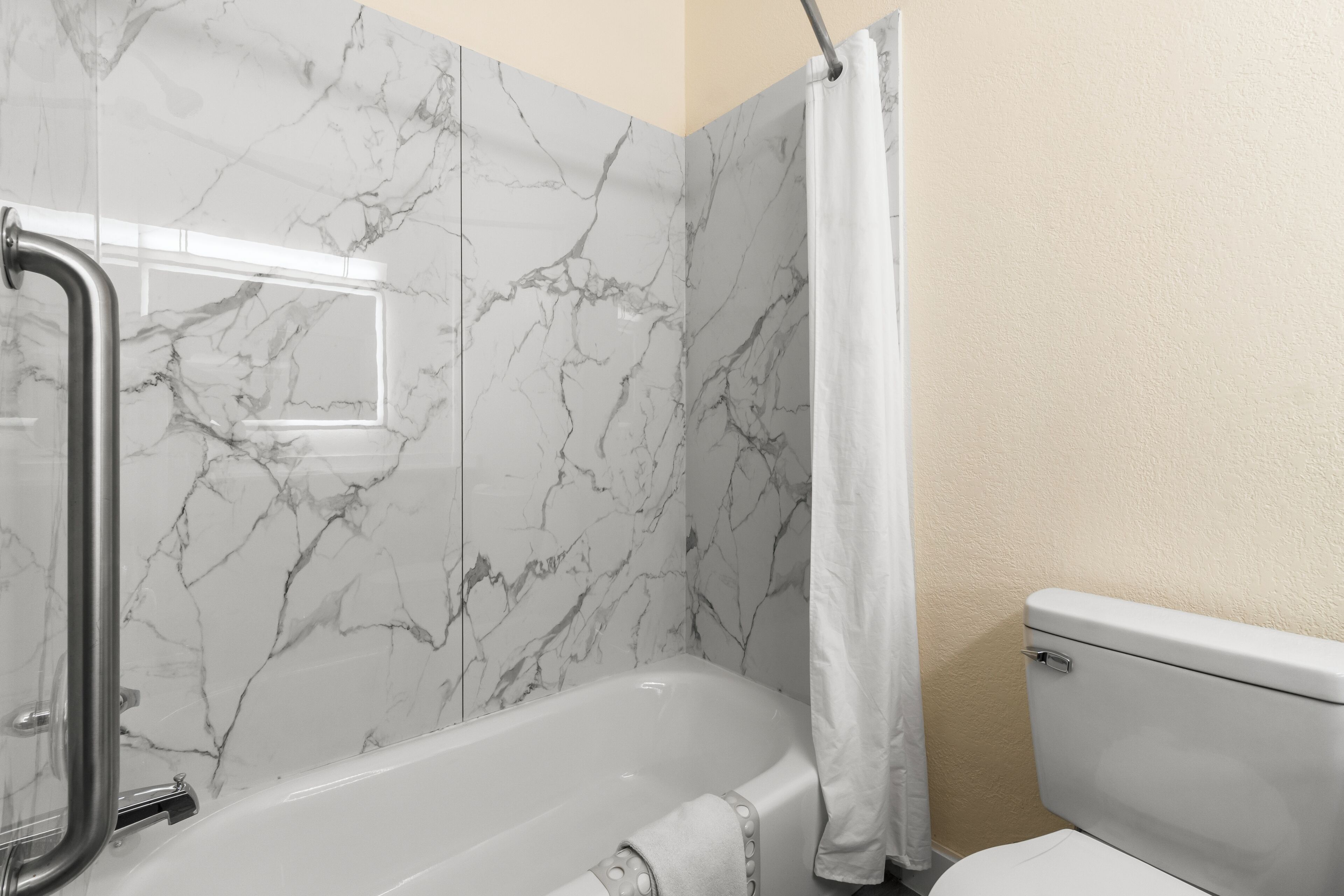 Un baño con pared de mármol, bañera, inodoro y cortina de ducha.