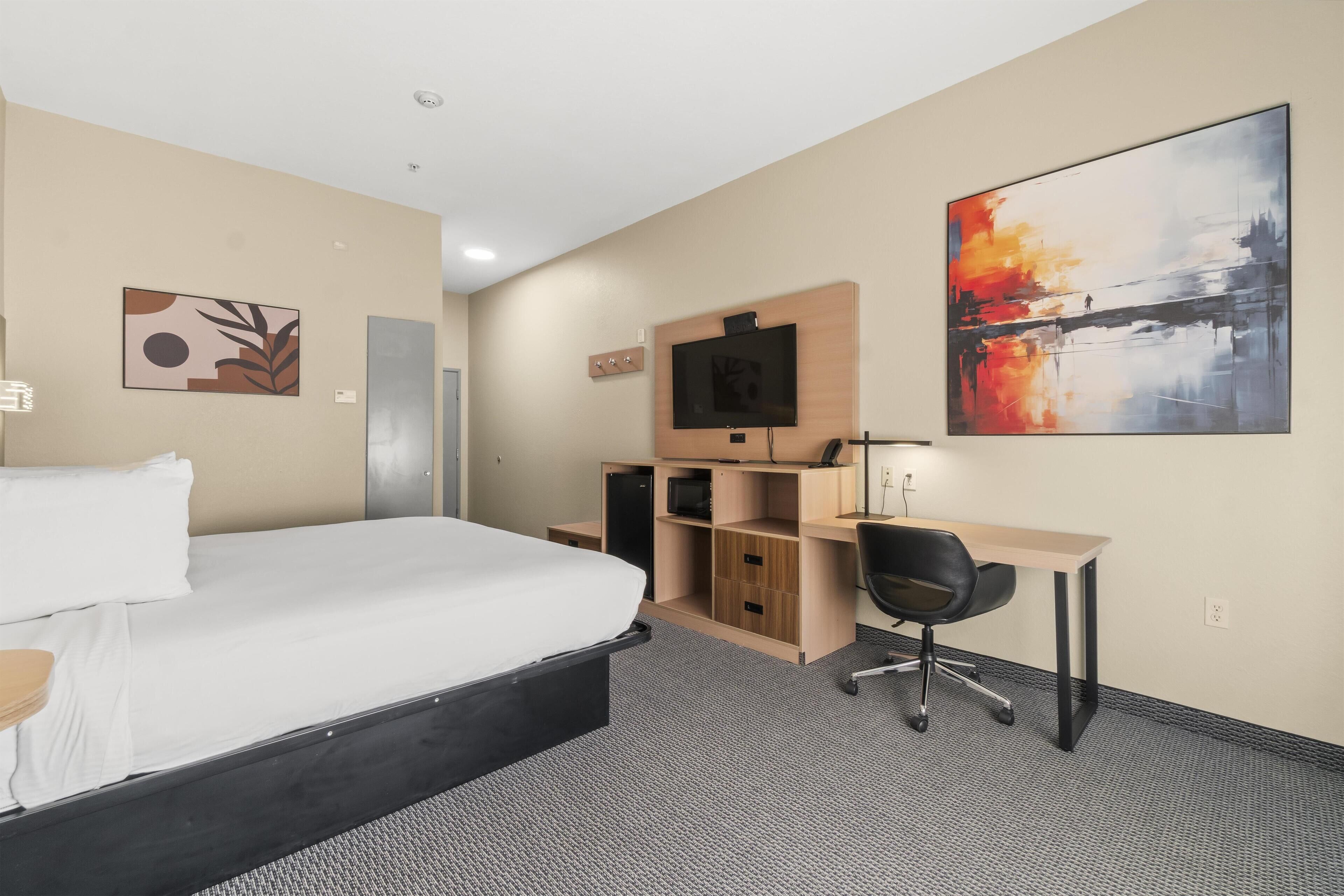 A hotel room with a bed, a desk, a chair, a TV, and artwork on the walls.
