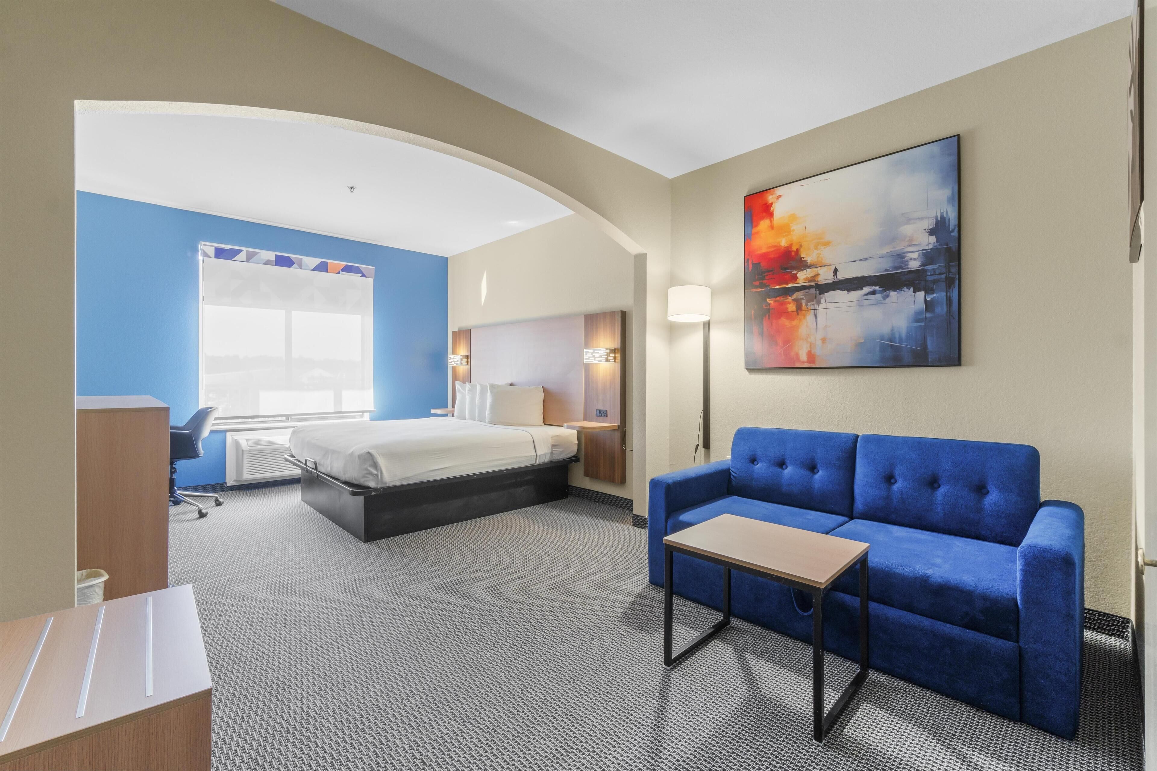 Een hotelkamer met een bed, een blauwe bank, een bureau en een schilderij aan de muur.