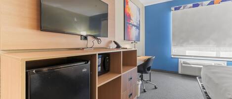 A hotel room with a bed, a desk with a chair, a television, a microwave, and a refrigerator.