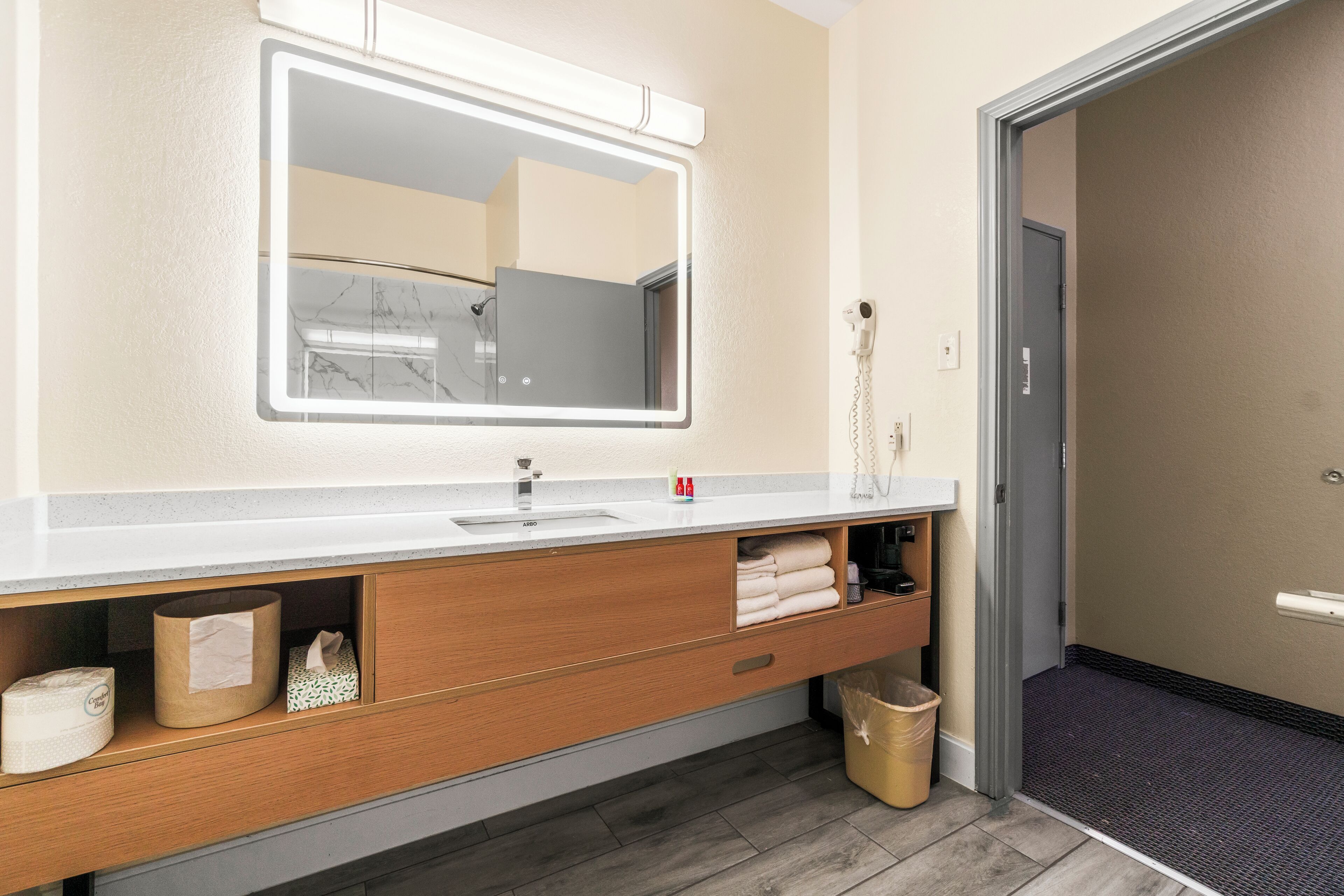 Un baño moderno con un espejo grande, un lavamanos blanco, tocador de madera y un perchero para toallas.