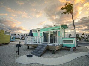 A turquoise mobile home with a porch and stairs, surrounded by other similar homes, under a cloudy sky.