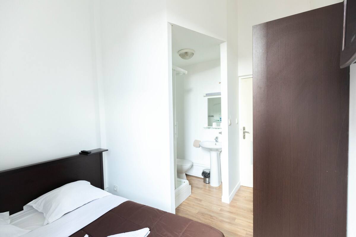 Une chambre d’hôtel avec un lit, une tête de lit en bois, un mur blanc et une porte donnant sur une salle de bain.