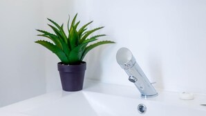 Ein Badezimmer mit einem weißen Waschbecken, einem modernen Wasserhahn und einem Topf mit Echte Aloe.