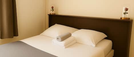 Una cama bien hecha con una toalla enrollada, un cabecero oscuro y dos cúpulas de vidrio con flores en la mesita de noche.