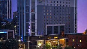 Un hotel moderno con un llamativo letrero de "Homewood Suites", que cuenta con una entrada central con puertas de vidrio y un estacionamiento al frente.