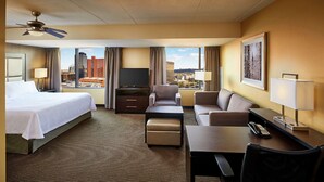 Habitación de hotel con cama, escritorio, sillón, televisor y vistas a la ciudad.