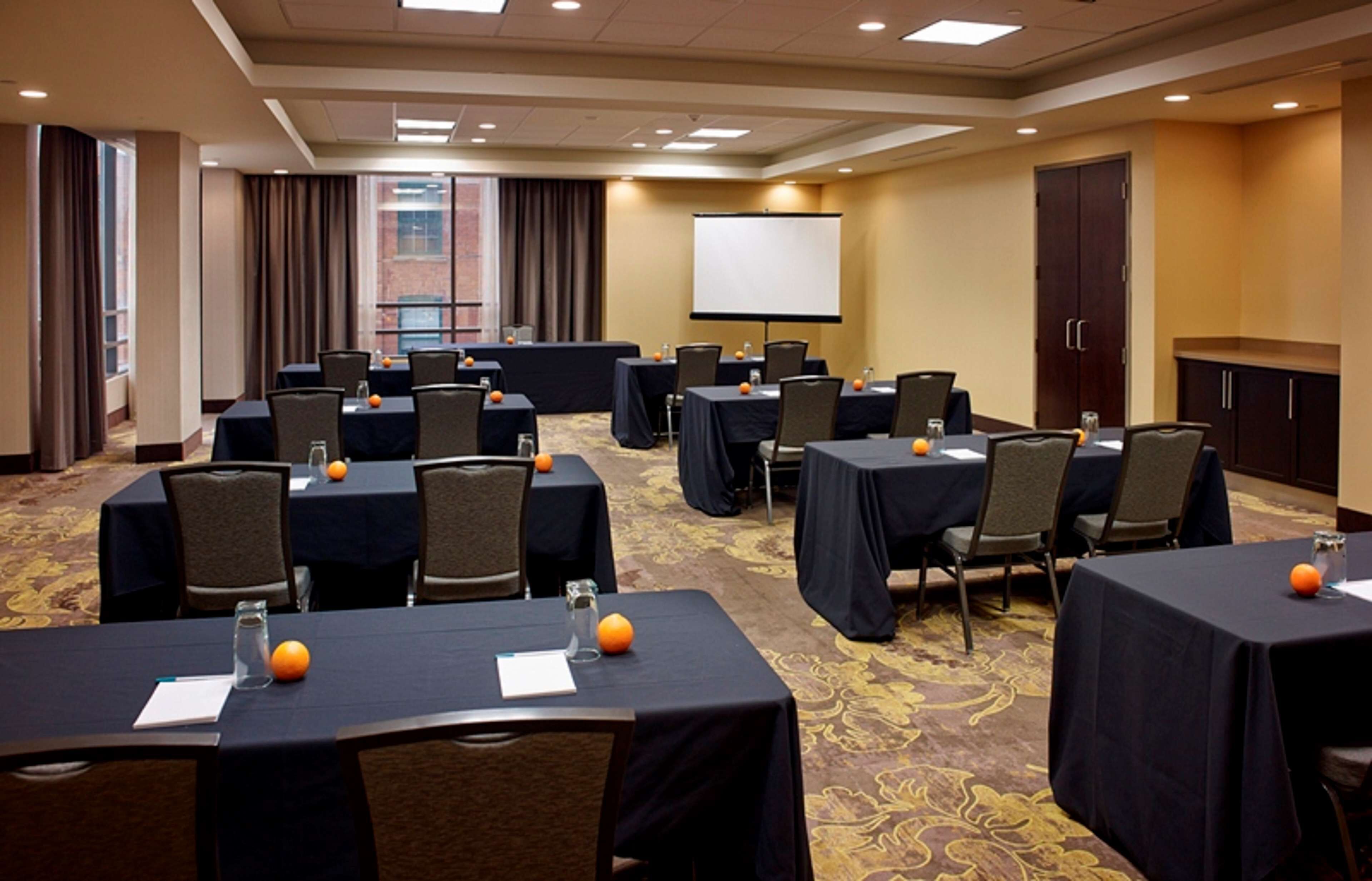 A conference room with multiple tables, chairs, and a projector screen.