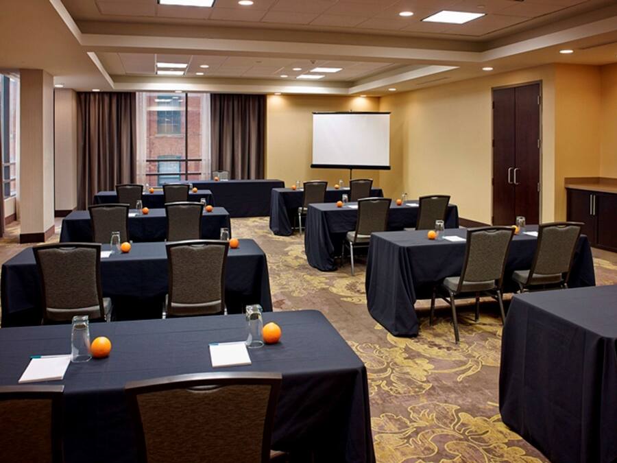 A conference room with multiple tables, chairs, and a projector screen.