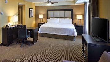A hotel room with a large bed, a desk with a chair, a television, and a ceiling fan.
