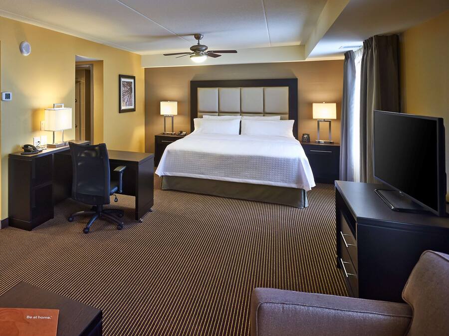 A hotel room with a large bed, a desk with a chair, a television, and a ceiling fan.
