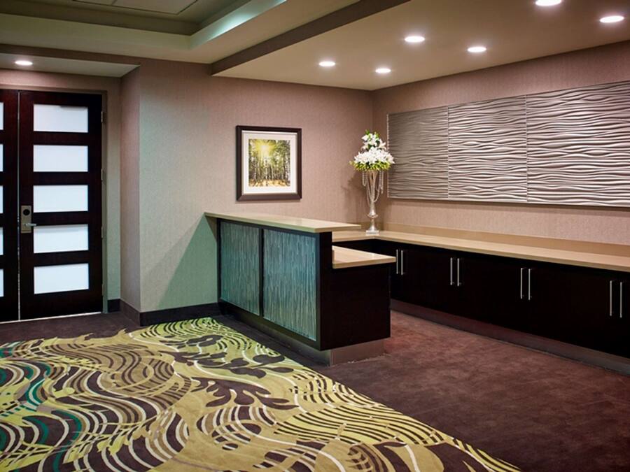 Habitación de hotel con alfombra estampada, un cuadro enmarcado en la pared, un florero con flores y un panel de pared texturizado.