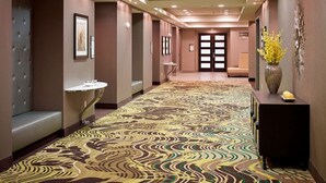 Un pasillo de hotel con alfombra estampada, un mostrador de recepción, un área de descanso y una puerta al final.