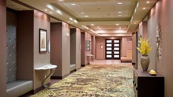 A hotel hallway with a patterned carpet, a reception desk, a seating area, and a door at the end.