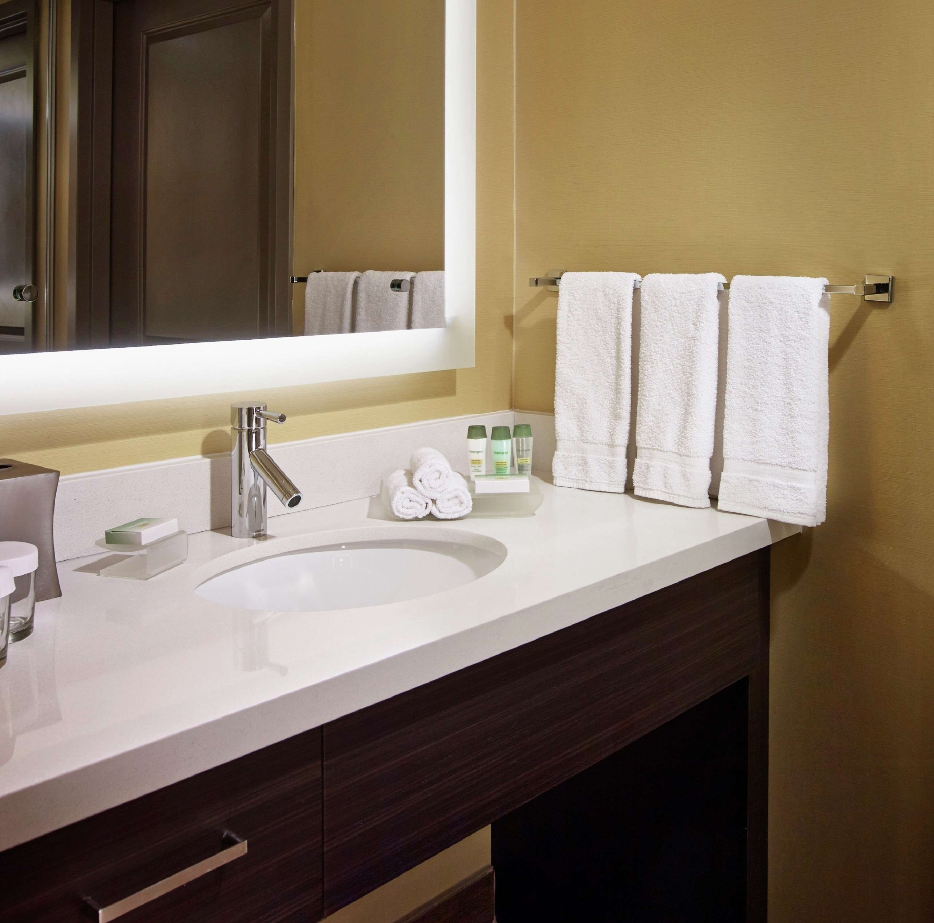 Un baño moderno con un espejo grande, un lavabo blanco y dos toallas colgadas en un perchero.