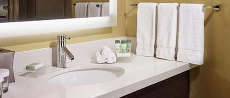 Une salle de bain moderne avec un grand miroir, un lavabo blanc et deux serviettes suspendues à un porte-serviettes.