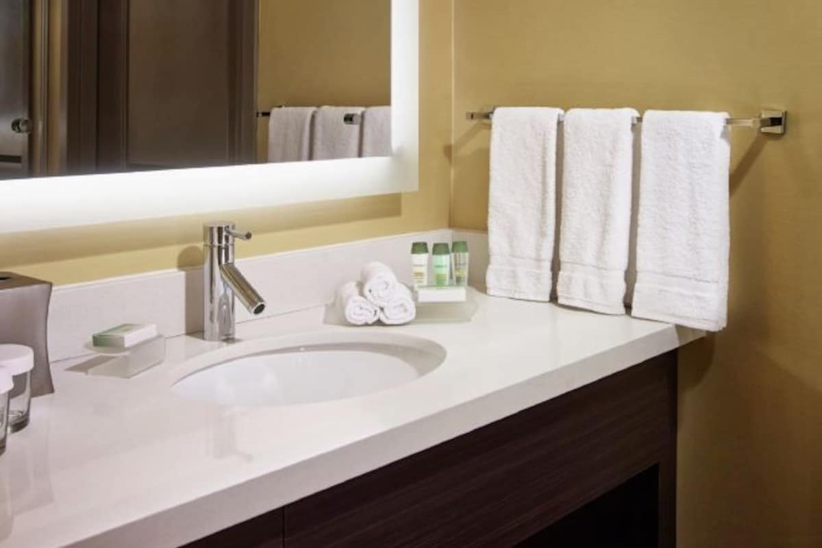 A bathroom with a white sink, a mirror, and three white towels hanging on a towel rack.