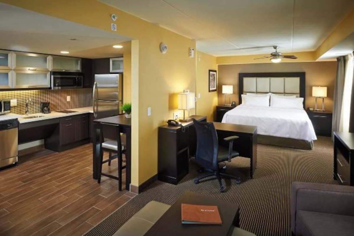 A hotel room with a bed, desk, chair, kitchenette, and a small seating area.