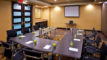 A conference room with long tables, chairs, a projector screen, and a small table with a laptop.