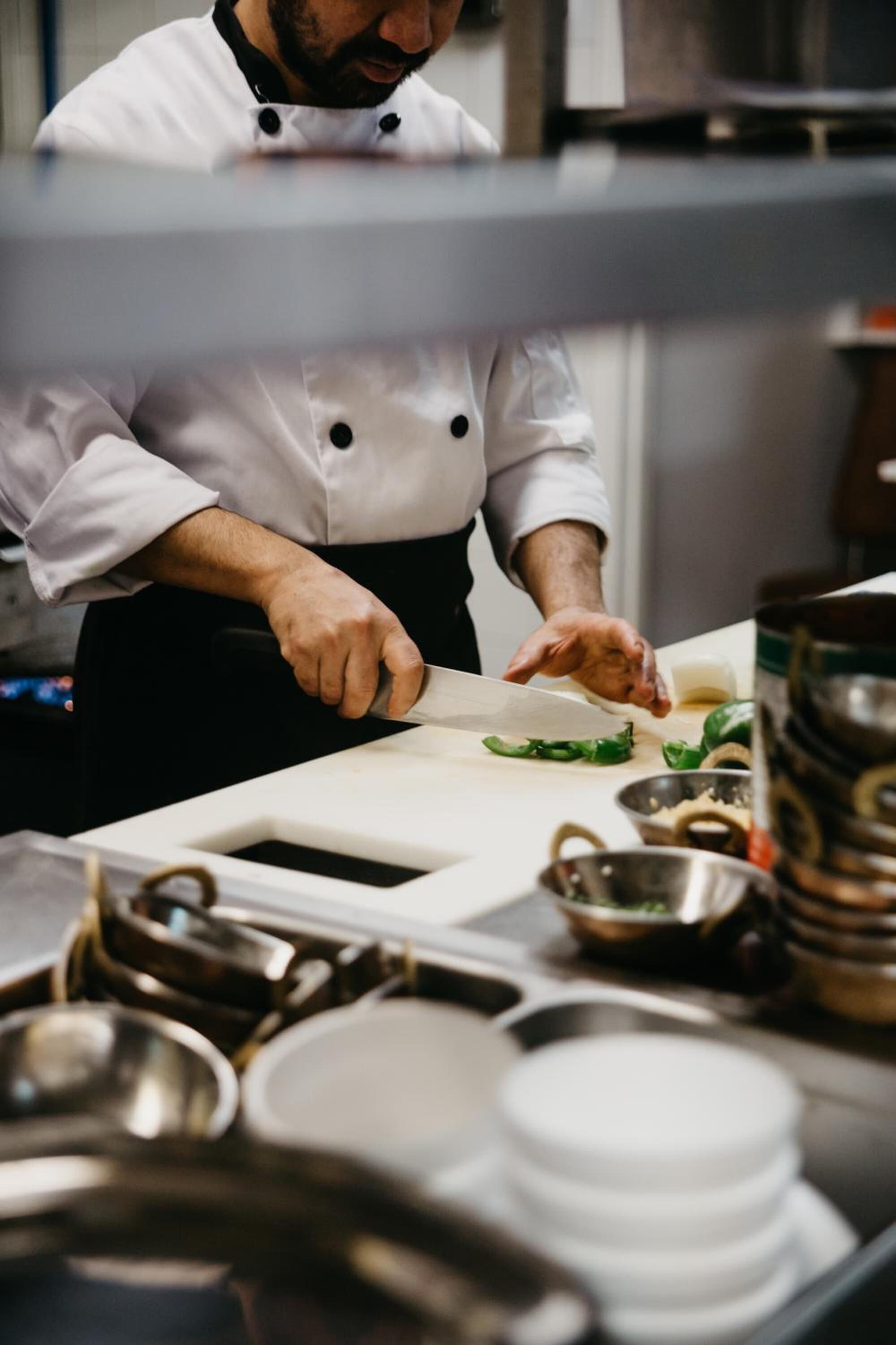 A chef in a white uniform cutting vegetables on a cutting board in a kitchen.