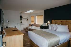 A hotel room with a large bed, a wooden desk, a bathroom with a bathtub, and a skylight. - Golden Village Lodge (Golden)