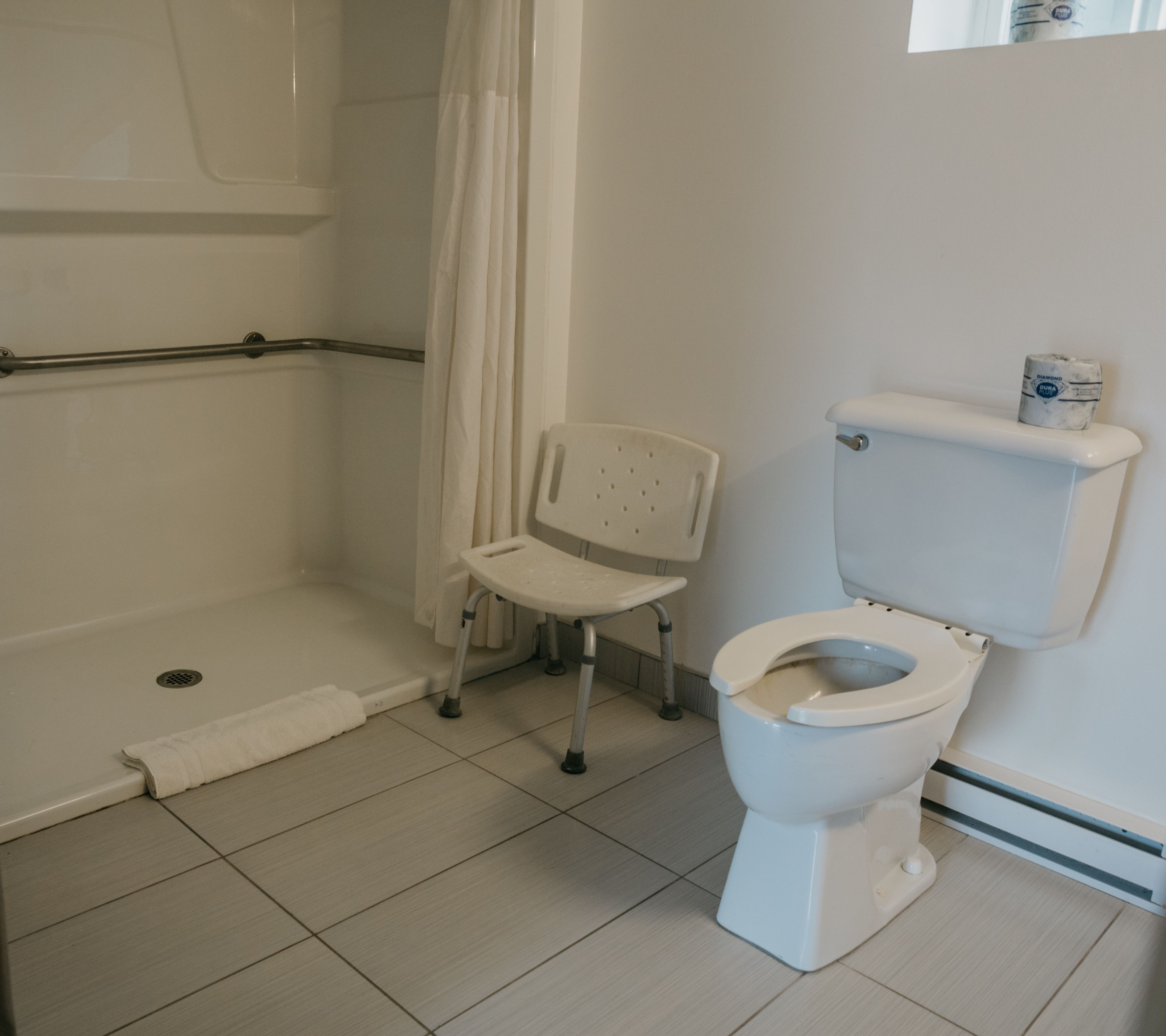A bathroom with a shower, toilet, and a wheelchair-accessible chair.