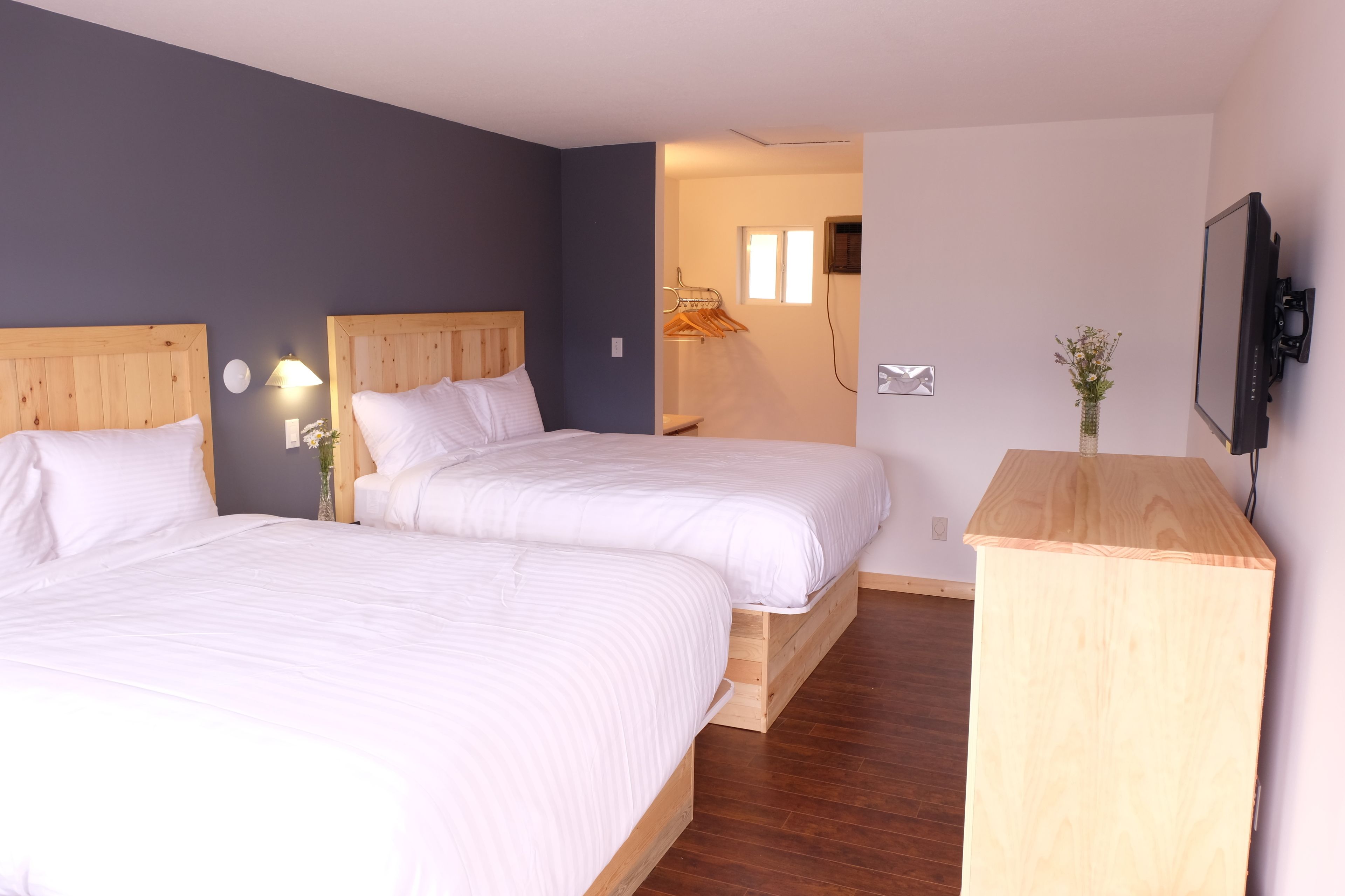 Habitación de hotel con dos camas, cabeceros de madera, una mesita de noche, un televisor y un mueble de madera pequeño.