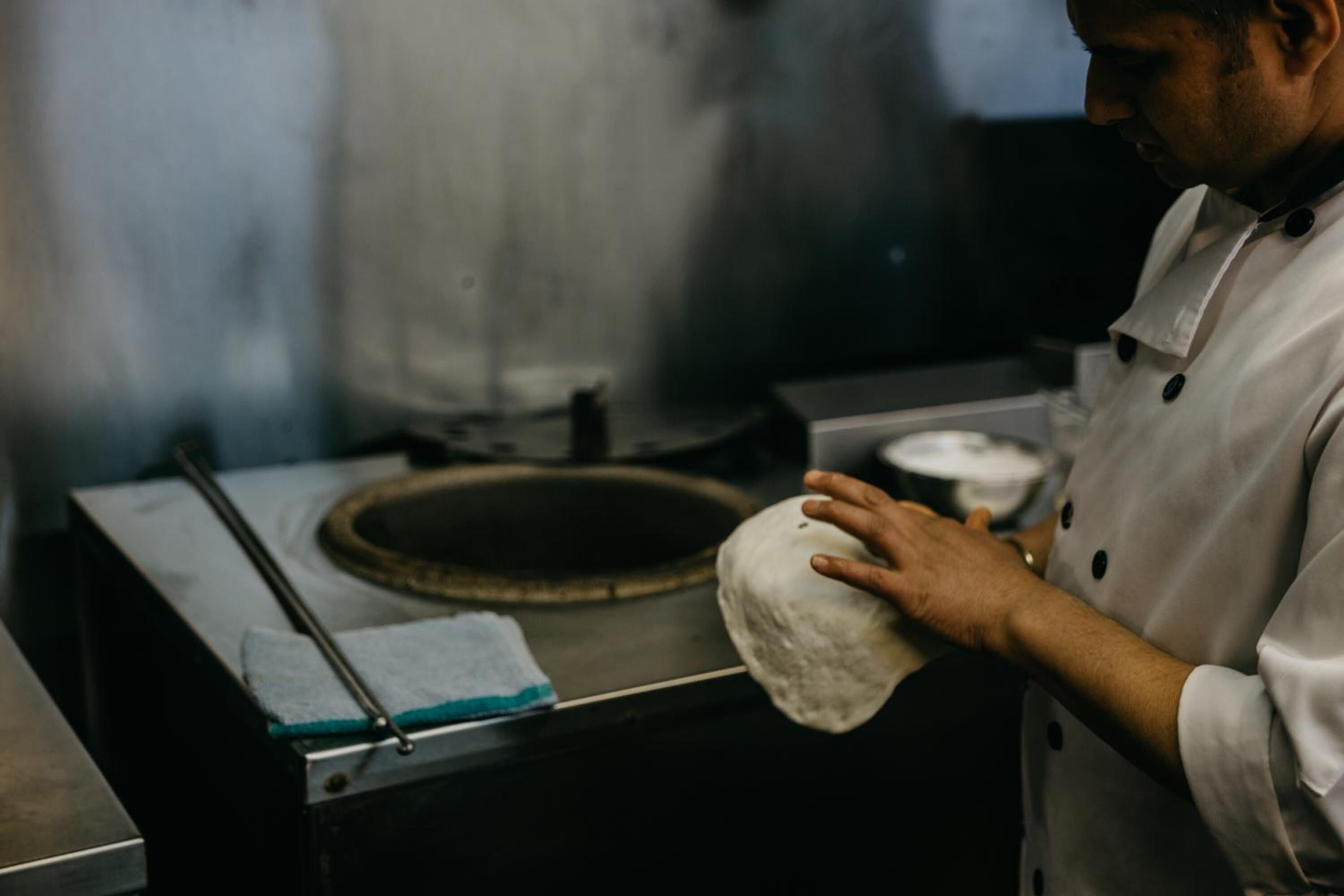 A chef holding a dough ball in a kitchen.