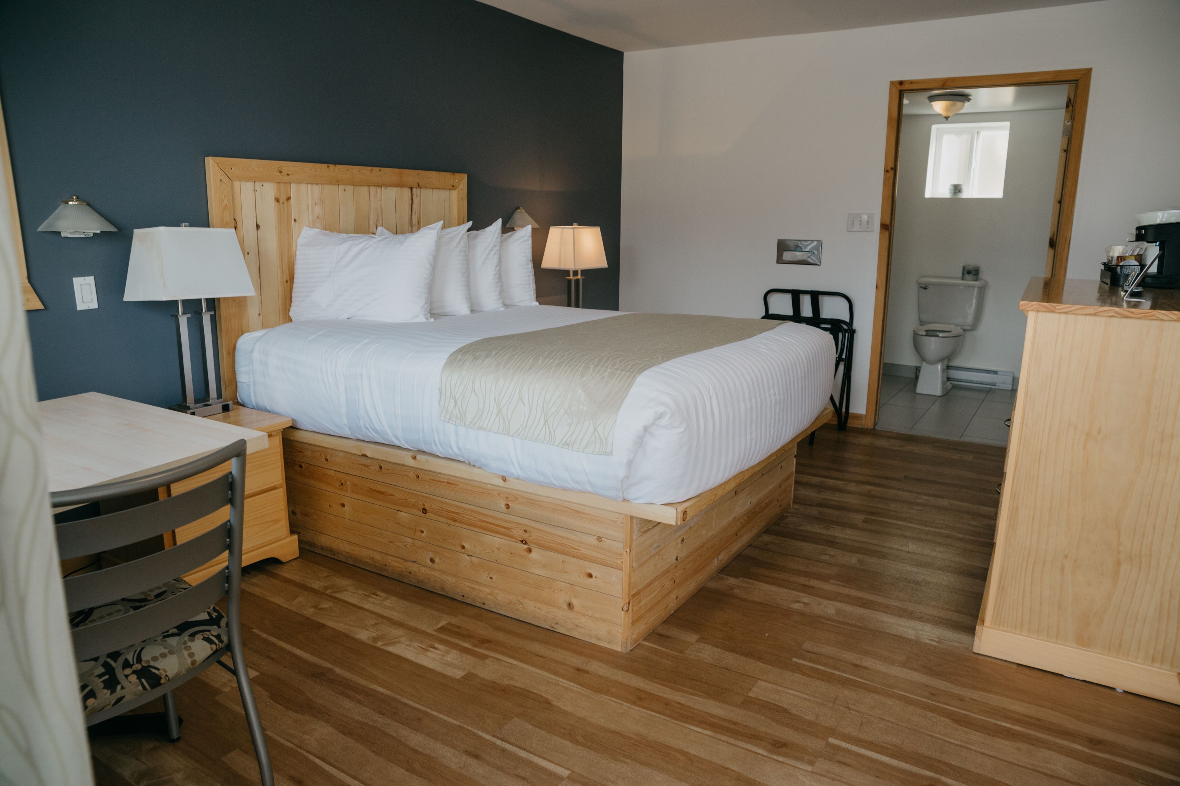Un dormitorio ordenado con una cama de madera, lámparas de noche, un tocador de madera y una silla.