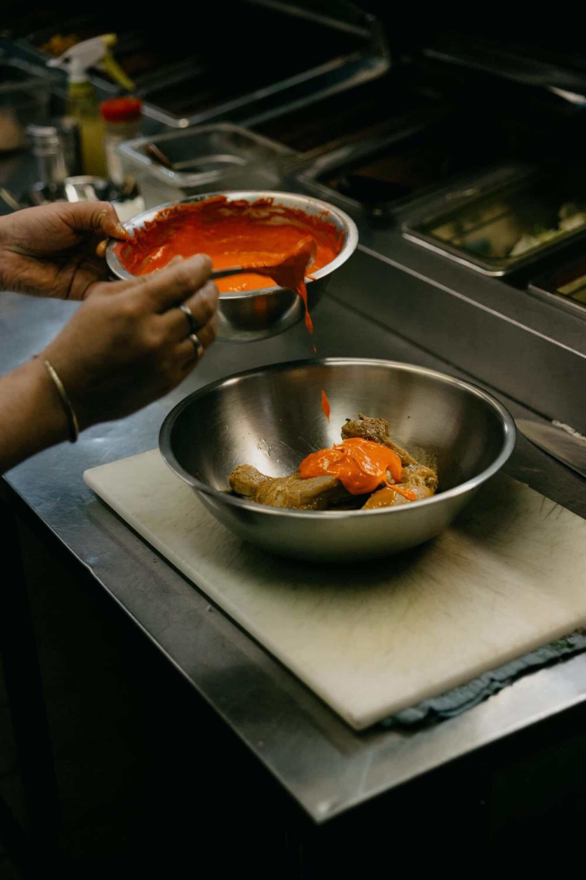 Una persona vertiendo salsa en un recipiente metálico sobre una encimera de cocina.