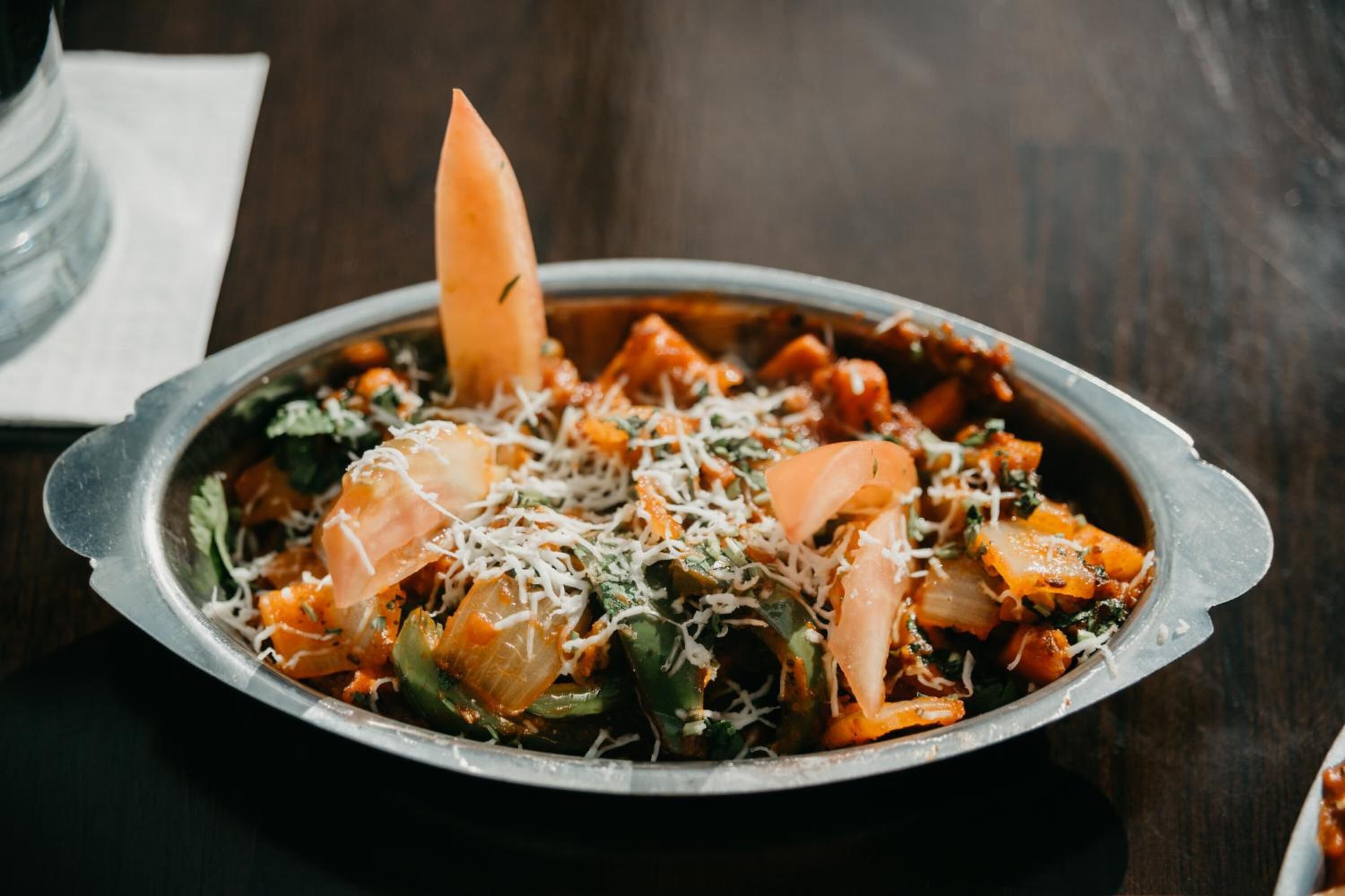 A dish with vegetables and cheese on a metal plate.