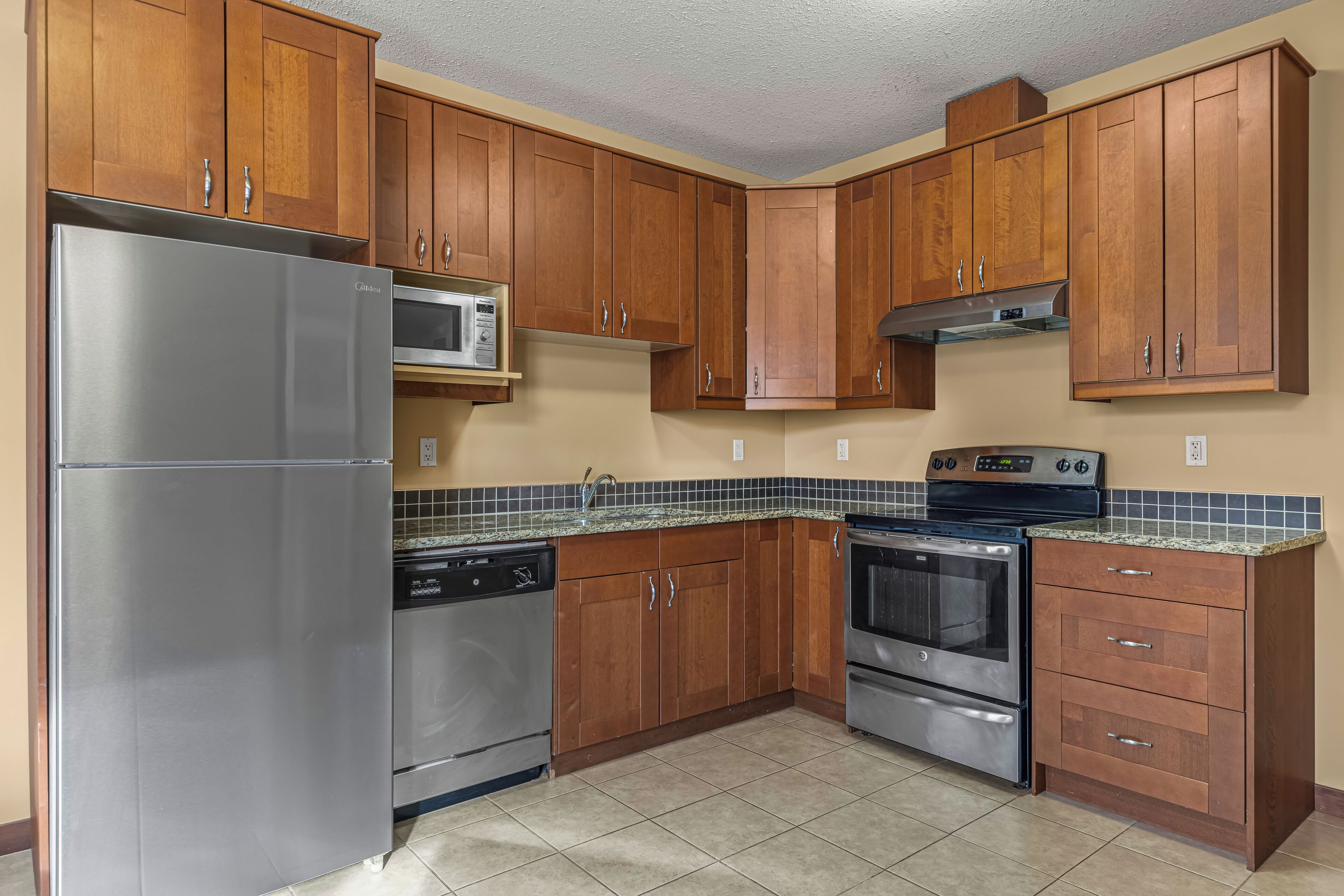 A kitchen with wooden cabinets, stainless steel appliances, and a tiled backsplash.