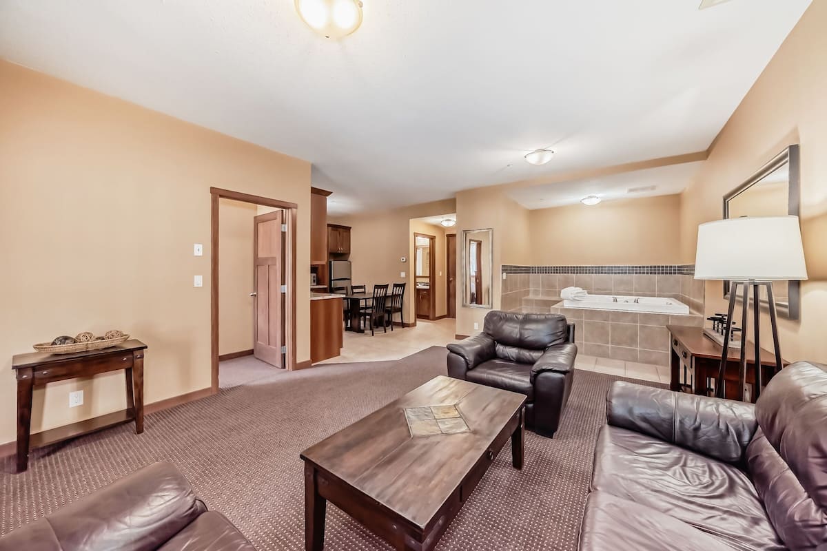 A living room with a brown leather sofa, a wooden coffee table, and a kitchen area in the background.