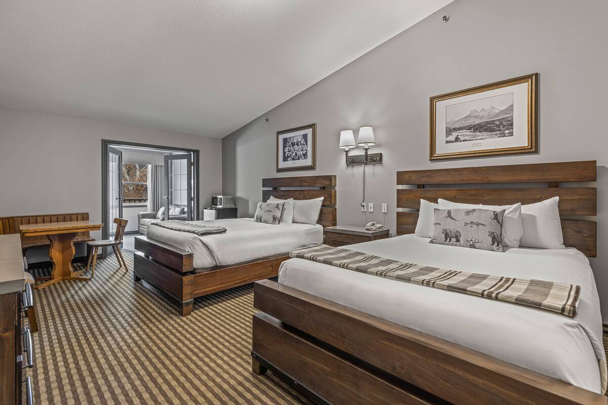 A hotel room with two beds, a desk, and a chair. There are two bedside tables with lamps, a large window, and a framed picture on the wall.