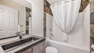 A modern bathroom with a large sink, a bathtub, and a toilet.