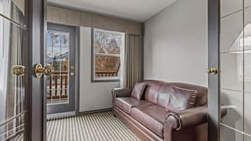 Una habitación con un sofá de cuero marrón, alfombra estampada, un ventanal con vistas a árboles y montañas, y una puerta con espejo y cortinas.