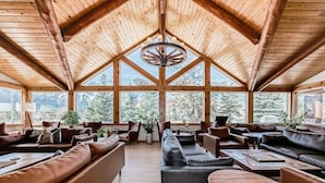 Una habitación amplia y luminosa, con vigas de madera, sofás de cuero y grandes ventanales que ofrecen vistas al exterior.
