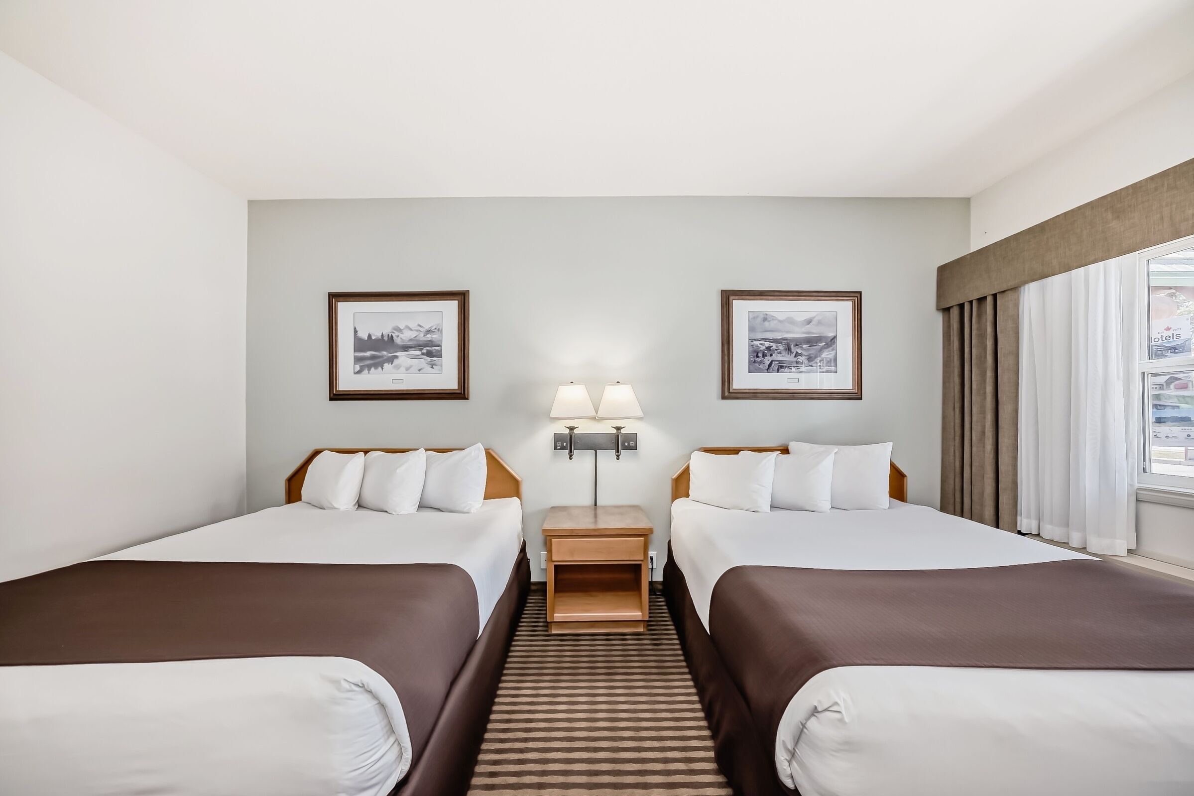 Una habitación de hotel con dos camas, una mesita de noche con lámparas y cuadros en las paredes.